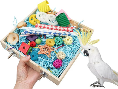 Hand holding parrot chew toys box filled with colorful bird-safe toys next to white cockatoo